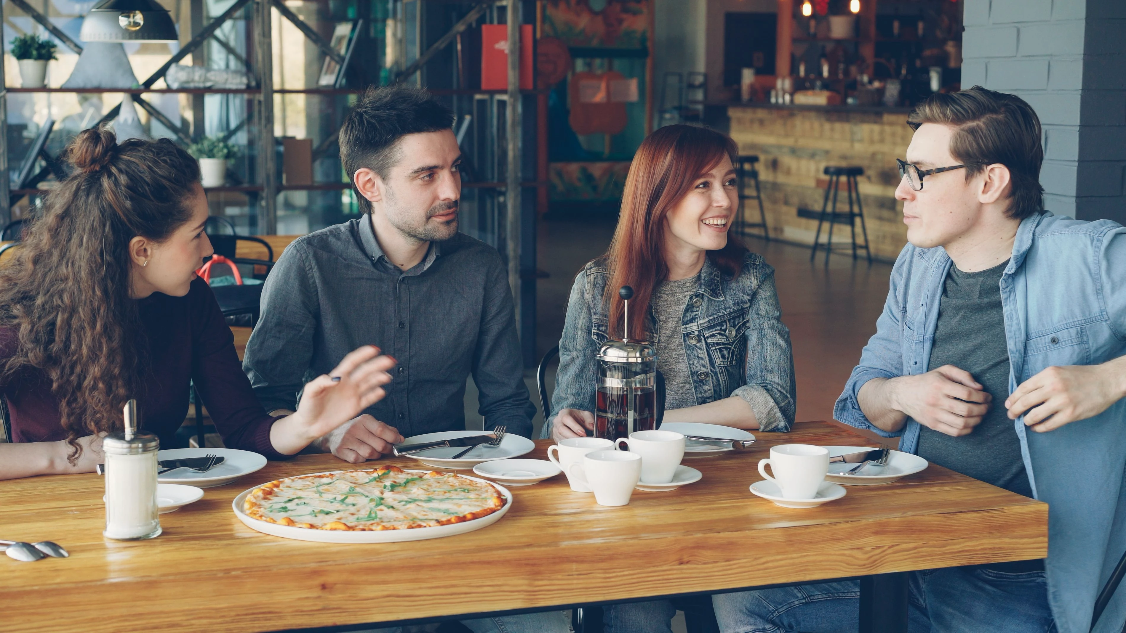 Friends talking around a cafe table with visible facial expressions and gestures — reading meaning from faces while listening